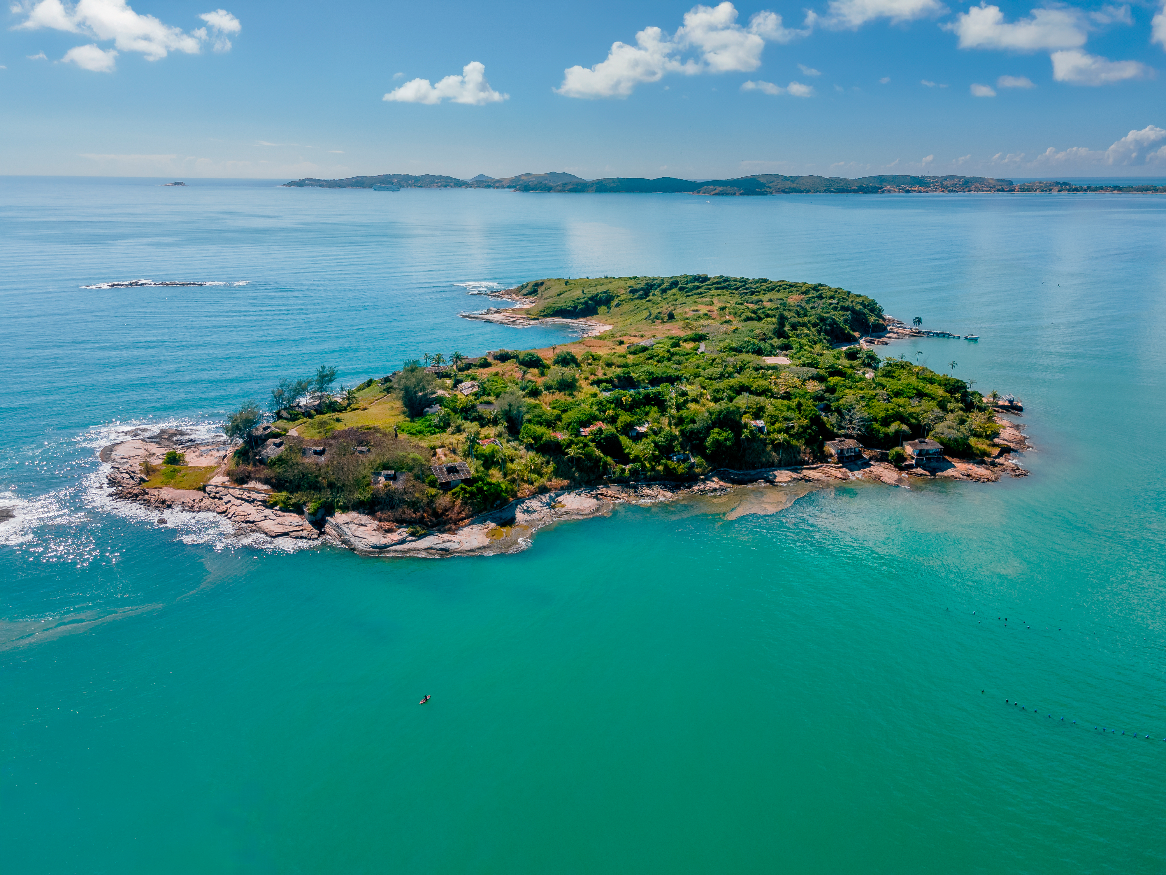 Vista aérea da ilha Nas Rocas sob o céu azul, cercada pelo mar de Búzios